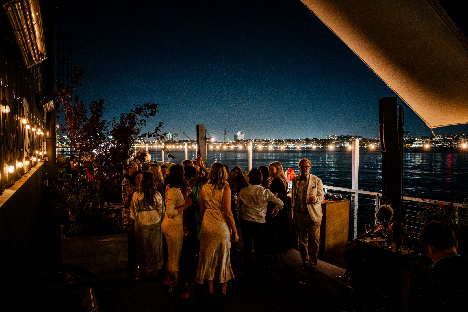 Guests gathered on a waterfront terrace at THE NAT GALA, with the New York skyline lit up at night