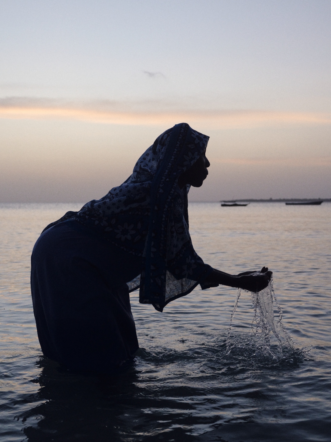 A woman silhouetted at dusk, wringing water from her hands as she stands in the sea