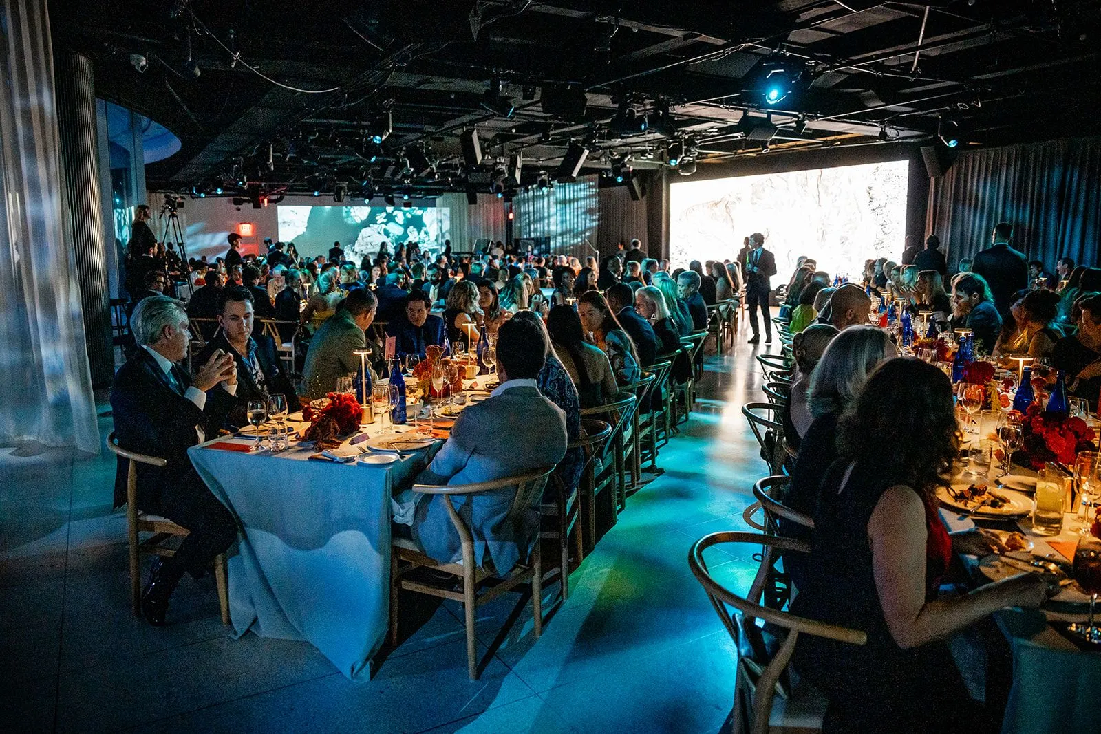 THE NAT GALA dining room at Halo 28, lit in deep ocean blue, with guests seated at long tables.